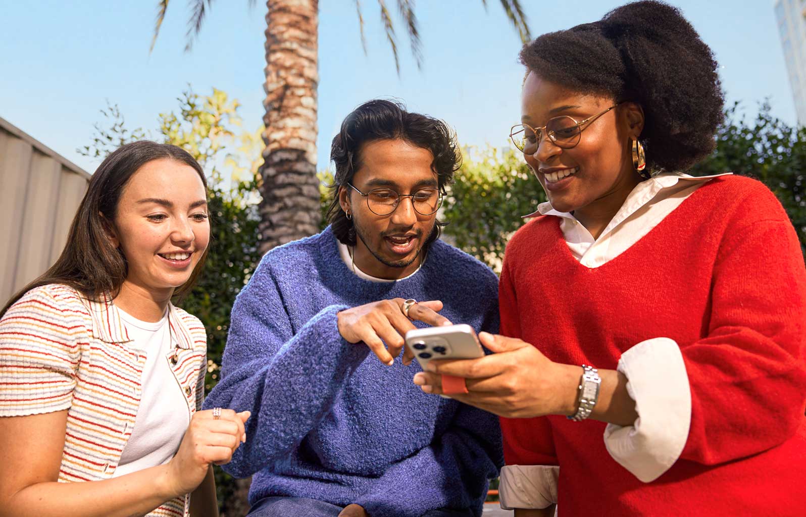 Three people interact with and watch a mobile phone.